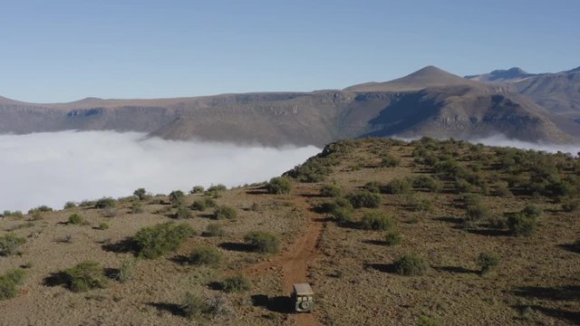4K aerial tilit up view of a safari 4x4 game drive vehicle driving  on a gravel road beautiful mountain scenery in the background