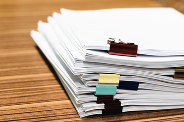 Close up pile of unfinished paperwork on office desk waiting to be managed and inspected. Stack of homework assignment with colorful paper clips. Report papers stacks. Business and education concept.