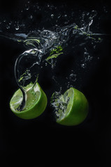 Fototapeta na wymiar Lime green fruit that is falling and has water spreading with a black background.