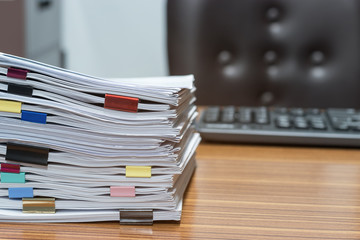 Close up pile of unfinished paperwork on office desk waiting to be managed and inspected. Stack of homework assignment with colorful paper clips. Report papers stacks. Business and education concept.