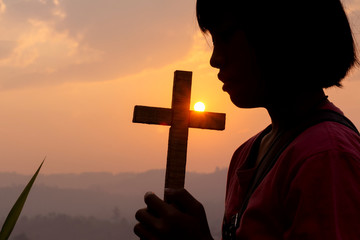 Silhouette of human praying to the GOD while holding a crucifix symbol at sunset