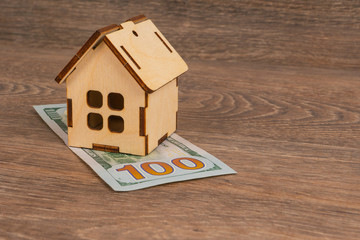 Obraz na płótnie Canvas expensive utilities cost concept with wooden house model and 100 dollar banknotes