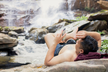 Man using cell phone on the rock at waterfall