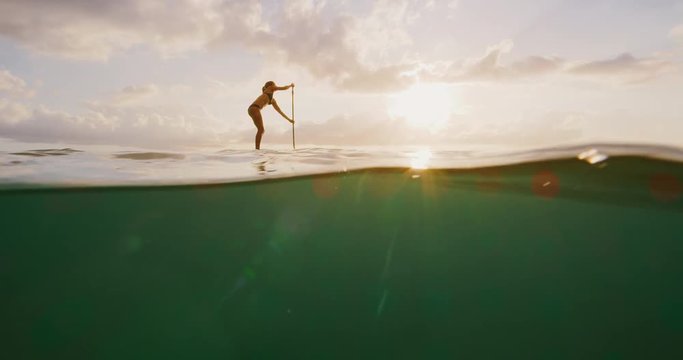 Over under shot of young happy active woman stand up paddling in the ocean at sunset, island ocean beach lifestyle, active healthy life