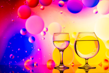 transparent glasses with water and oily drops on colorful background 