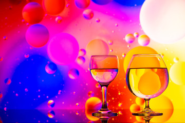 transparent glasses with water and oily drops on colorful background 
