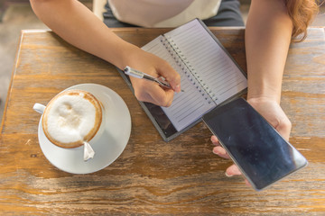 Top view of female hand writing note and using smartphone