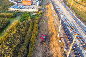 The bulldozer clears the space along the railway tracks. Raking of reeds by bulldozer © eleonimages