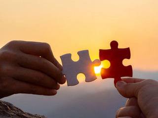 hands holding piece of jigsaw puzzle at sunset background. teamwork concept