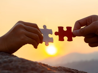 hands holding piece of jigsaw puzzle at sunset background. teamwork concept
