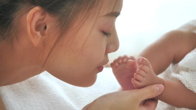 Beautiful young asian mother kissing her baby's feet while sleeping on the bed