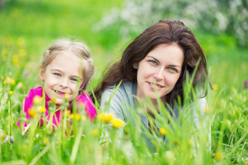 Mother and daughter lying on green summer grass with blooming yellow flowers