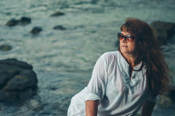 Fototapeta premium a woman in sun glasess on a rock looking into the distance against the sea