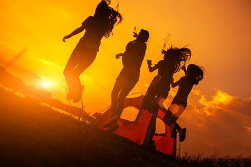 Silhouette Group of women party with drink bottles and jumping enjoy travel camping,trekking in vacation time at sunset.