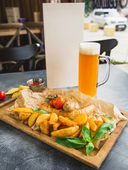 Grilled sausages with fried potatoes and pickled tomato on wooden board and glass of beer
