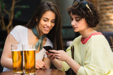 Two girls chatting while having a beer. Long haired and short haired girl drinking beer. 