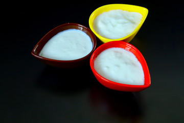 Yogurt in colorful bowls on black table top view