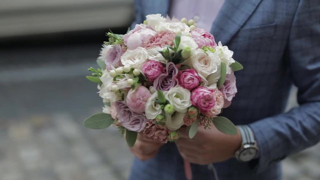 Groom with wedding bouquet in his hands on the street. Pink shirt, blue jacket