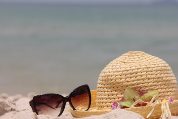 Beach scene. Sun straw hat and sunglasses lying on the sand on the beach
