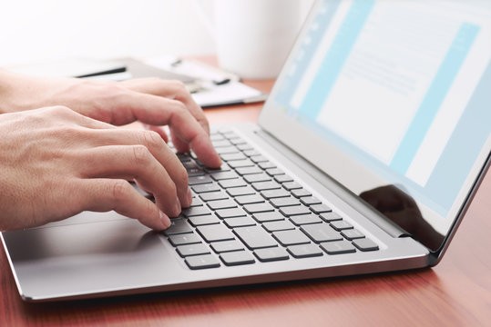 Businessman sending email by laptop. Close up of hand using computer at table.