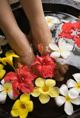 Obraz na płótnie Canvas Feet of woman in flower bath, Woman legs in bath tube with flowers spa relaxation body care therapy concept.