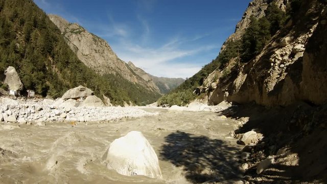 small ashrams on banks of Ganges channel in stony gorge in high mountains Himalaya powerful stream of brown water from melted snow with mud spring cirrus clouds in blue sky