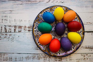 rainbow colorful easter eggs on beautiful ornamental plate on wooden table