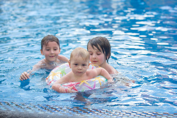 Fototapeta na wymiar Adorable happy little child, toddler boy, having fun relaxing and playing with his older brothers in a pool on sunny day during summer vacation