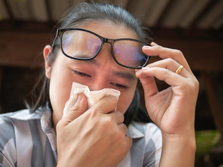 Asian young woman waring glasses with holding tissue and blowing her nose. Runny nose. Flu season. Health and medical concept.
