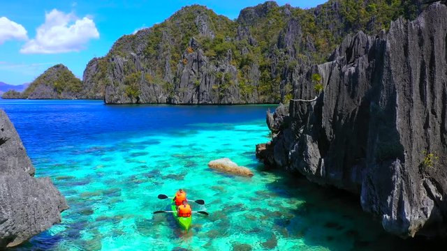 Aerial view flying over amazing rocks and tropical coral reef lagoon. Man and woman Kayak are sailing on the sea. Coron, Busuanga, Philippines.