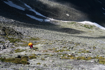 Tourist climbs up the stones in the mountains. Going up the rocky moraine