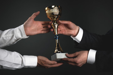 Award ceremony concept. Businessman is giving a golden cup award trophy to a winner. First place...