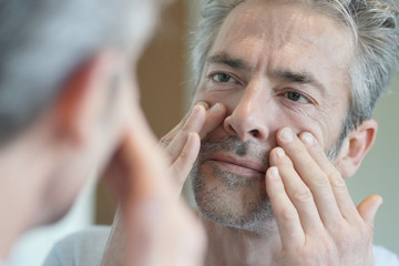 Portrait of mature handsome man looking in mirror at home