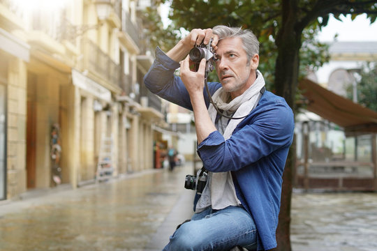 Mature photographer taking photos with vintage camera in European old town