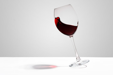 Red wine splashes in a glass on white background