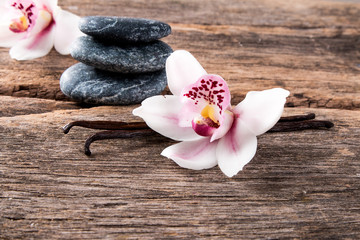 Dried vanilla pods and orchid flower on wooden background.