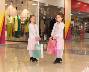 Two young twin sisters with shopping bags walking at the mall