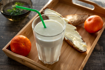 Morning milk glass. Buttermilk dairy drink breakfast on wooden desk. Tangerine, bread, butter.