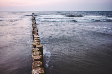 Wooden sea breakwater at sunset, color toning applied, long exposure.