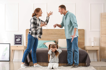 Fototapeta premium Sad little girl covering ears while her parents are arguing at home