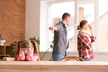 Sad little girl and her quarreling parents at home