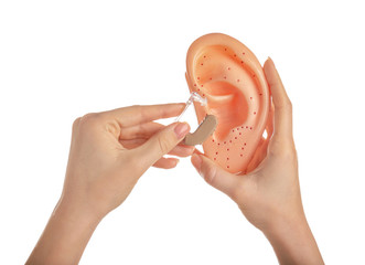 Female hands with hearing aid and model of ear on white background