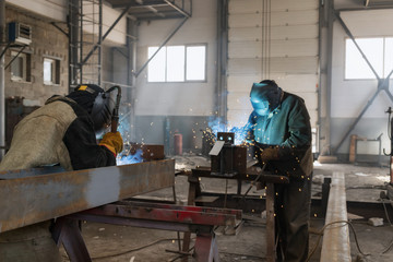 Two welders are welding metal structures mechanized semi-automatic welding