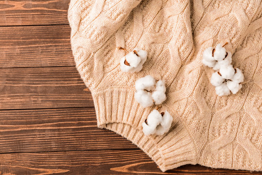 Cotton flowers with knitted sweater on wooden background