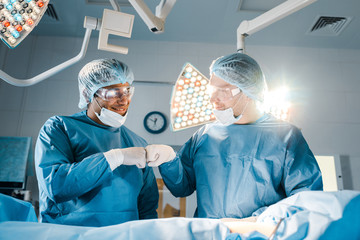 nurse and surgeon in uniforms doing gesture and smiling in operating room