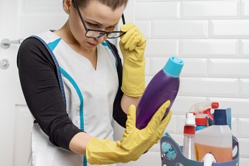 Adult woman doing cleaning with detergents. Woman in glasses, professional uniform in bathroom,...