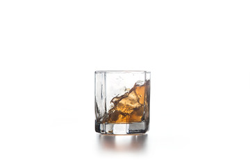 Whiskey splash in glass with ice on light background..