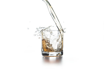 Whiskey pouring into glass with ice on light background..