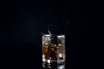 Fototapeta na wymiar Whiskey splash from the fallen ice cube into glass with beverage isolated on black background..