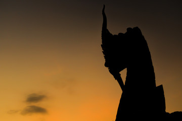 Silhouette of Thai Naka, big snake, serpent statue on yellow  sky at dawn. Mythical creature in Buddhism belief. Traditional Thai style architecture.